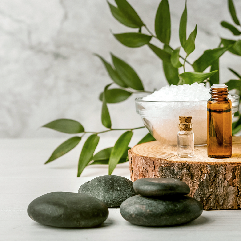 Aromatherapy setup with stones, essential oils, and a bowl of salt on a wooden block.