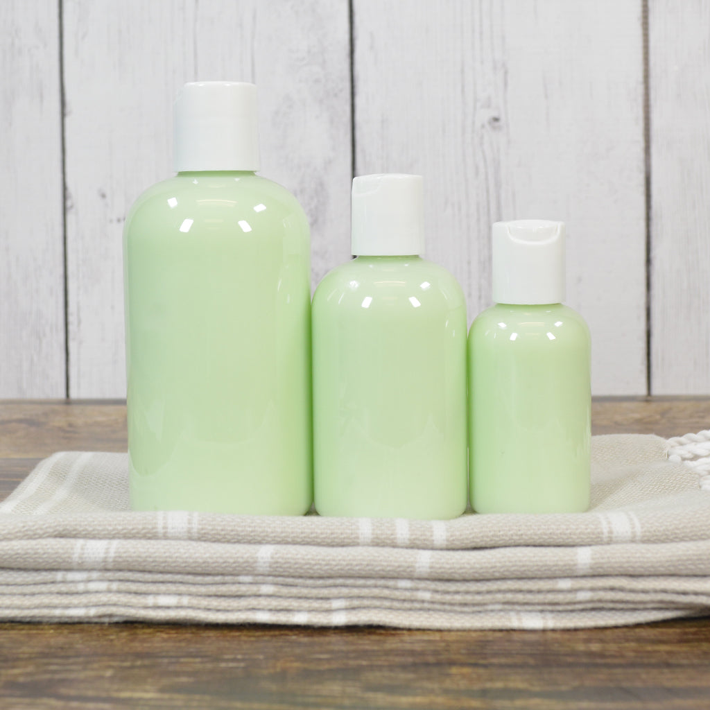 Three green bottles with white caps on a wooden surface with a light wooden panel background.