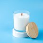 White candle in a glass container with a wooden wick and lid on a blue background - Zoom Thumbnail Media 1