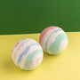 Two colorful bath bombs on a yellow surface with a green background