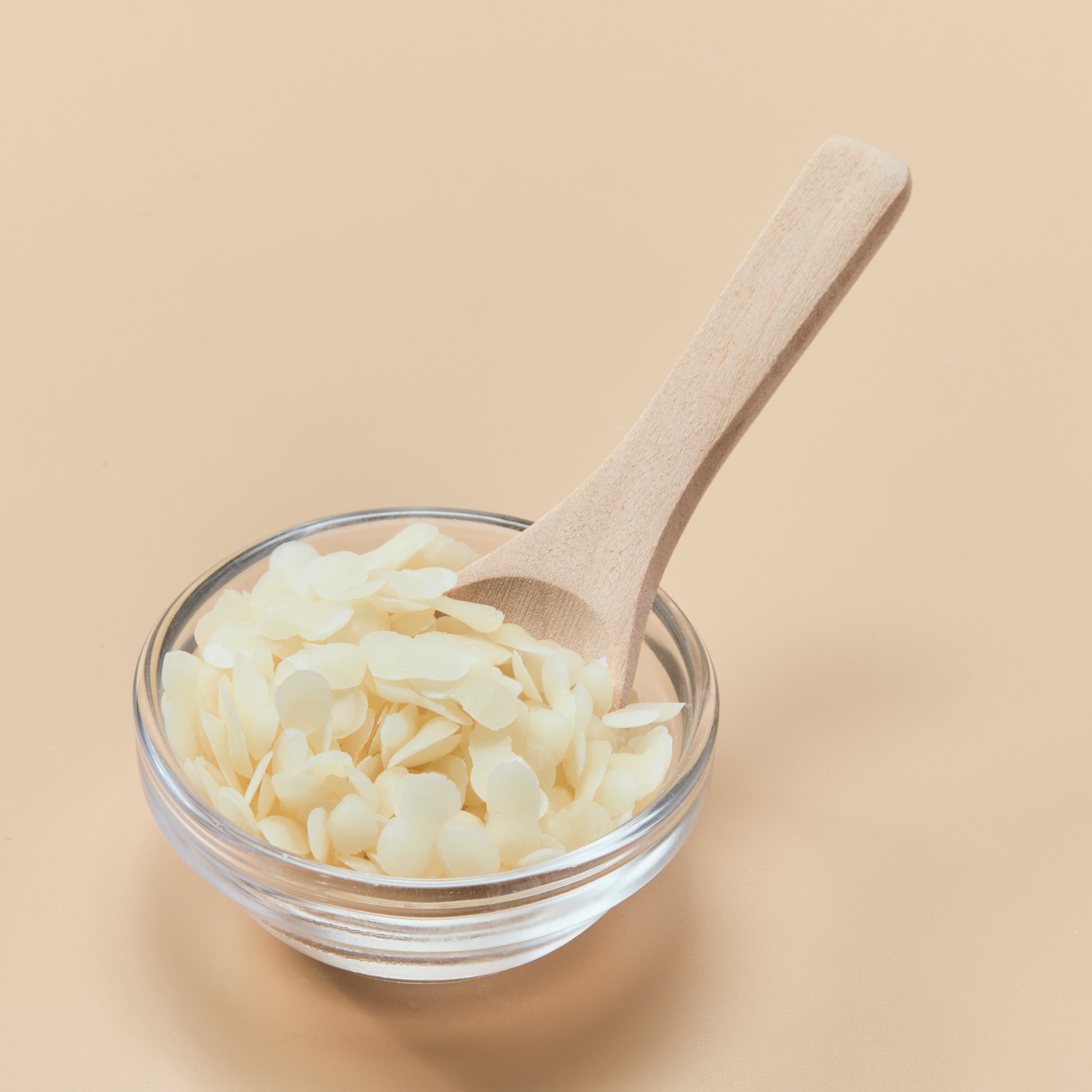Glass bowl with wax melts and a wooden spoon on a beige background