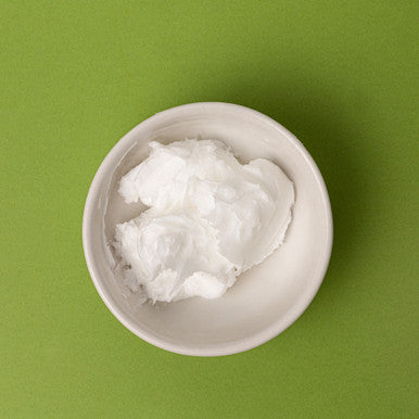 White bowl filled with coconut oil on a green background