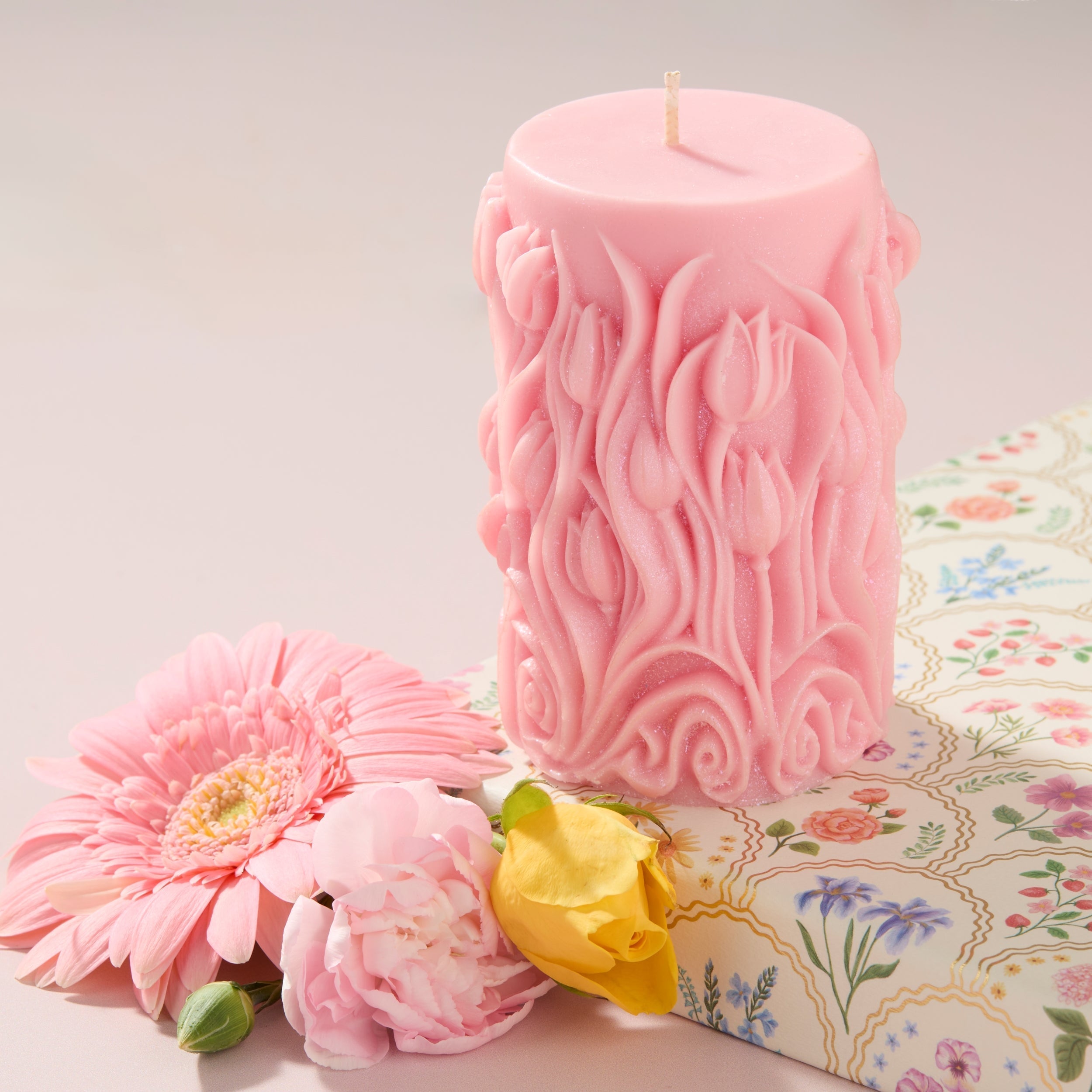 pink candle with flower detail next to flowers