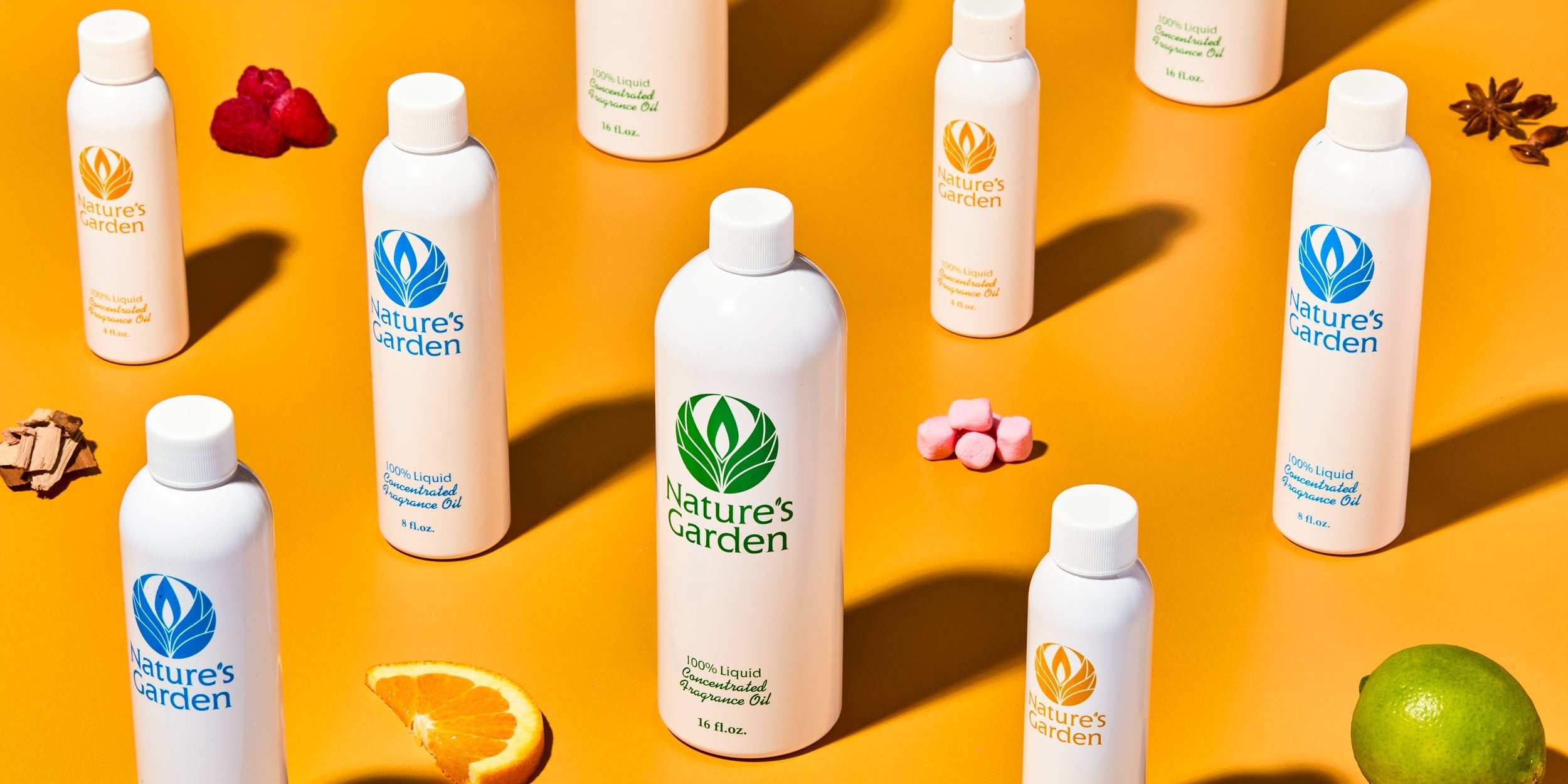Nature’s Garden fragrance oil bottles arranged on orange background with scent accents including orange slice, lime, raspberries, pink marshmallows, cinnamon bark, and star anise.