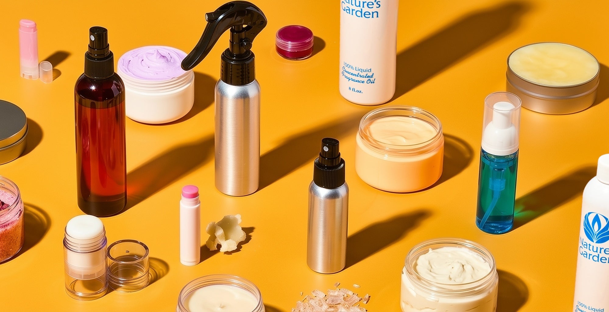 Assorted skincare and home care products arranged on a bright yellow background: jars of cream, spray and pump bottles, lip balms, scrub, candles, and wax cubes casting sharp shadows.