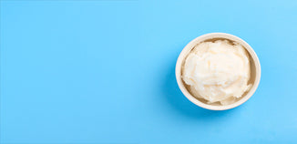 White ceramic bowl filled with creamy white tallow on a bright blue background with ample copy space.