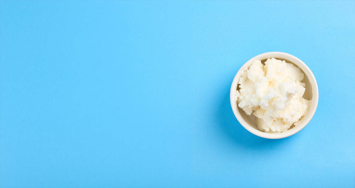 Top-down view of a small white bowl filled with a creamy white butter-like substance on a bright blue background.