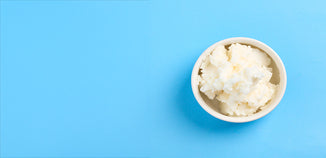 White lard or body butter in a white ceramic bowl on a light blue background.