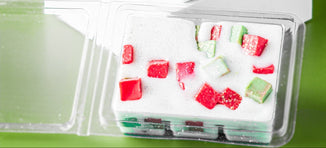 Chunky Christmas clamshell wax melts with red, green, and white pieces arranged in a clear plastic mold on a green surface, evoking a festive holiday theme.