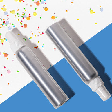Two silver spray bottles with white nozzles on a blue and multicolored confetti background