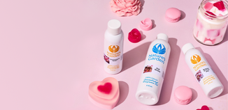 Flat lay of Nature’s Garden fragrance oil bottles and pink heart-shaped soaps on a soft pink background with candy-inspired accents.