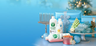 Festive holiday display featuring Nature’s Garden fragrance bottles surrounded by blue wrapped gifts, sparkling ornaments, a menorah, and soap shaped like a Christmas tree.