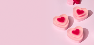 Pink heart-shaped melt and pour soaps arranged on a pastel pink background with smooth shadows.
