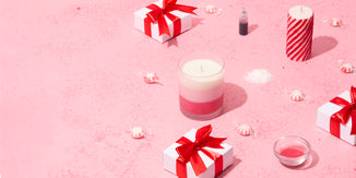 Peppermint-themed holiday display featuring pink and white candles, gift boxes tied with red ribbons, peppermint candies, and glitter scattered across a pink surface, evoking a festive and cheerful mood.