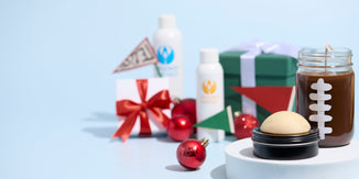 Nature’s Garden fragrance oils and soapmaking supplies displayed in a snowy winter scene. The image features three Nature’s Garden bottles with green, orange, and blue logos surrounded by handcrafted blue candles, soap, and whipped body butter on a snow-like surface against a sparkling blue background.