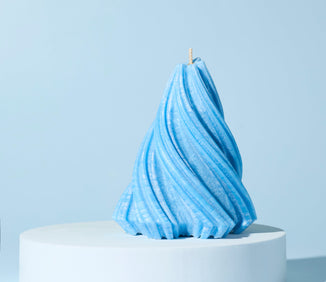 Blue sculpted candle with a twisted, textured design displayed on a white pedestal against a light blue background.