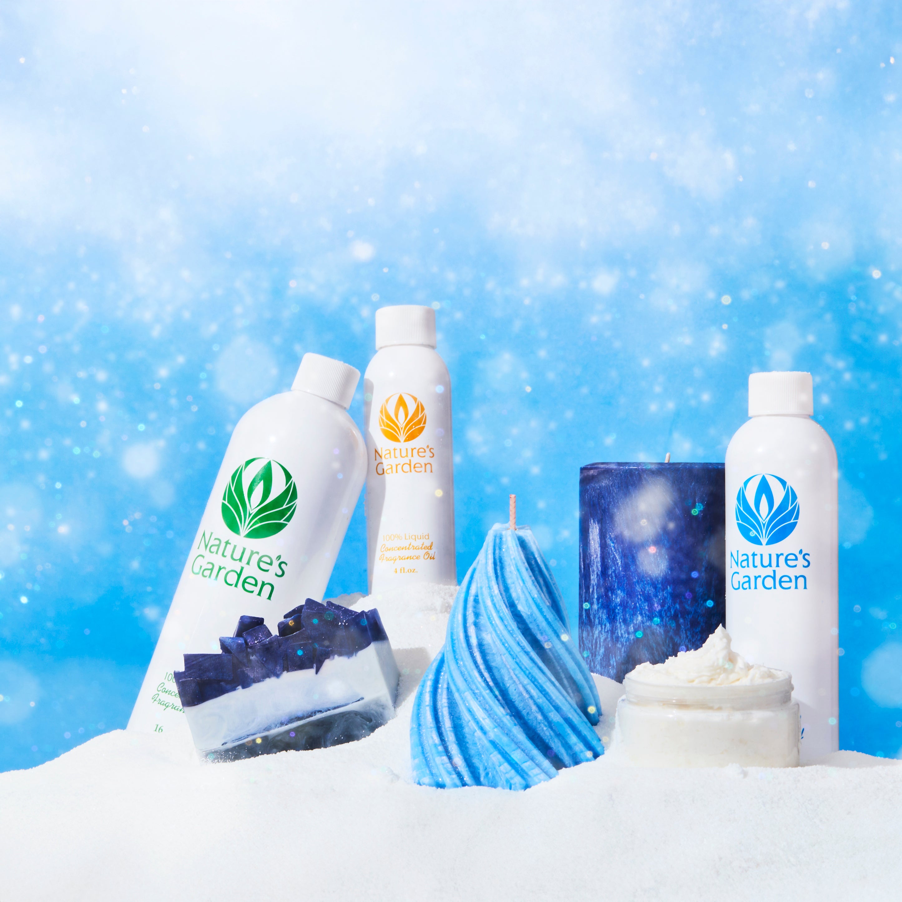 Nature’s Garden fragrance oils displayed in a snowy winter scene with handcrafted blue soap, candles, and whipped body butter. The products sit on a snow-like surface against a sparkling blue background, evoking a cool and festive atmosphere.