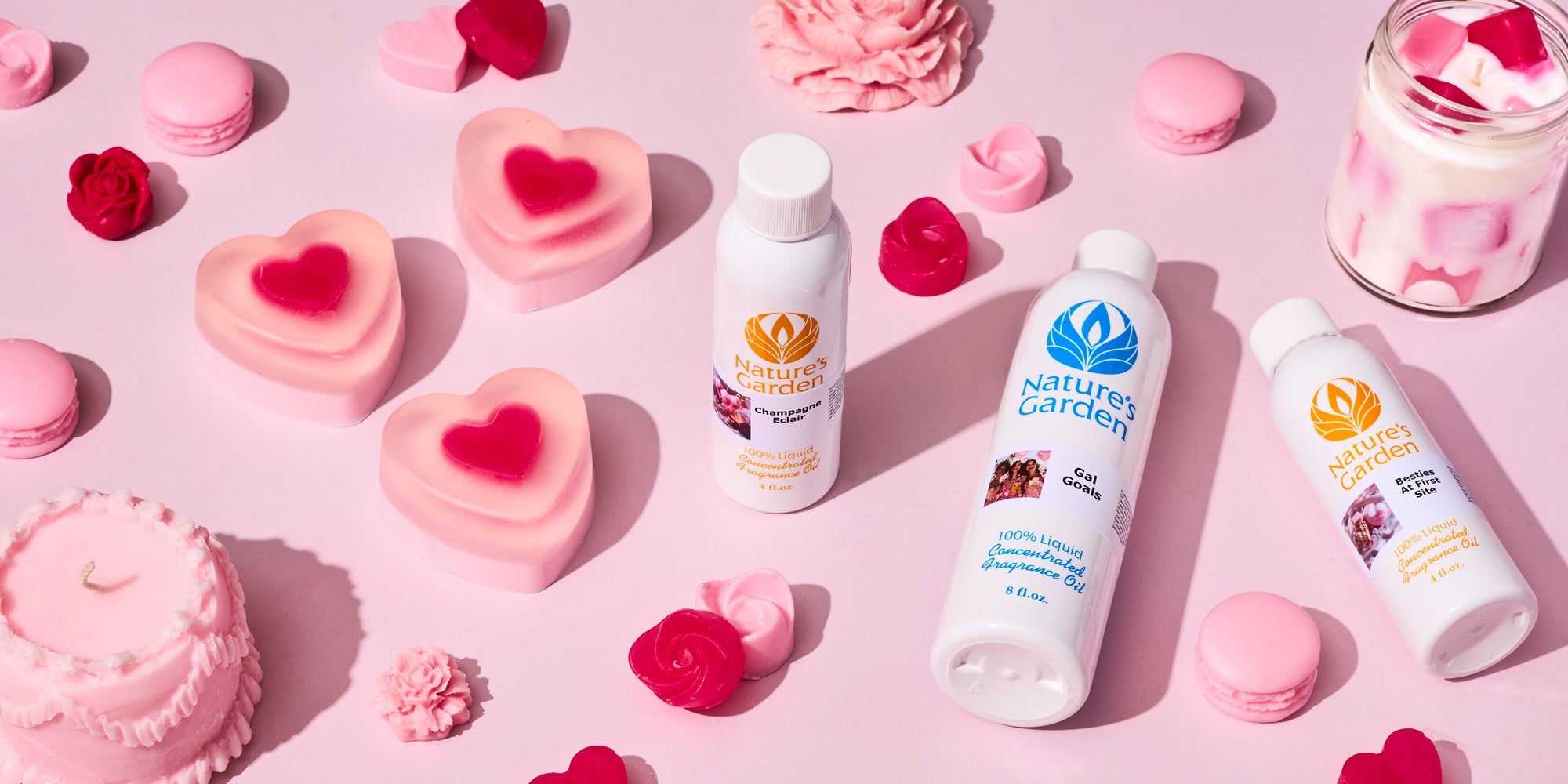Flat lay of pink and red heart-shaped soaps, wax melts, and a layered candle surrounding Nature’s Garden fragrance oil bottles on a soft pink background, styled for a Valentine’s or Galentine’s theme.