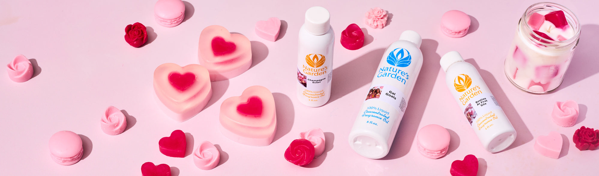 Flat lay of pink and red heart-shaped soaps, wax melts, and a layered candle surrounding Nature’s Garden fragrance oil bottles on a soft pink background, styled for a Valentine’s or Galentine’s theme.