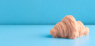 Plain croissant placed on a smooth blue surface with a matching blue backdrop.