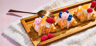 Mini croissants topped with icing and fresh berries arranged on a wooden tray with a fork.