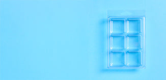 Clear wax melt clamshell with six medium square cavities and a hinged lid on a bright blue background.
