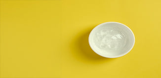 Clear cosmetic gel in a white ceramic bowl on a bright yellow background.