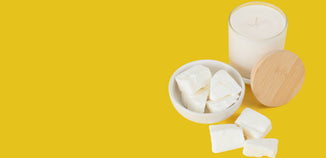 White candle with wooden lid and white wax melts arranged on a bright yellow background.
