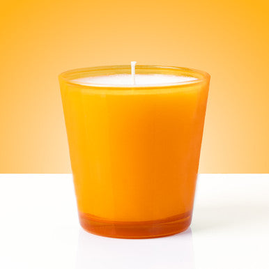 Orange candle in a glass container on a white surface with an orange background