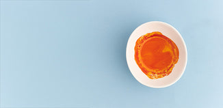 Amber-colored liquid oil in a white ceramic dish on a light blue background.