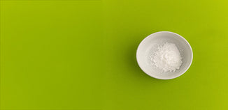 Fine white cosmetic powder in a white ceramic bowl on a bright green background.