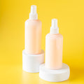 Two pink spray bottles on white stands against a yellow background