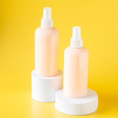 Two pink spray bottles on white stands against a yellow background