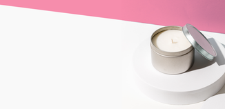 Tin massage candle with lid resting nearby on a white platform against a pink and white background.