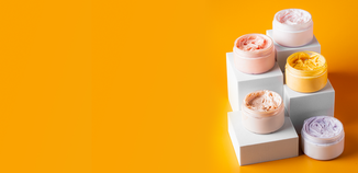 Colorful whipped lotion sitting on white blocks building up on an orange background.