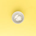 White cream in a small white bowl on a yellow background