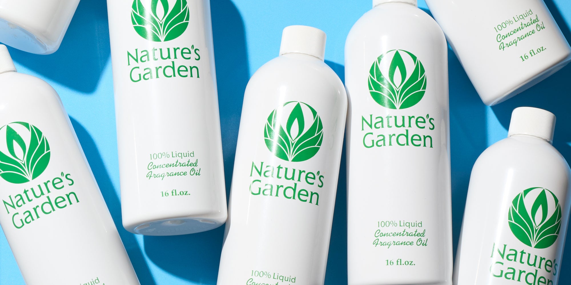 White Nature's Garden fragrance oil bottles arranged on a bright blue background, with green leaf logos and product labels visible.