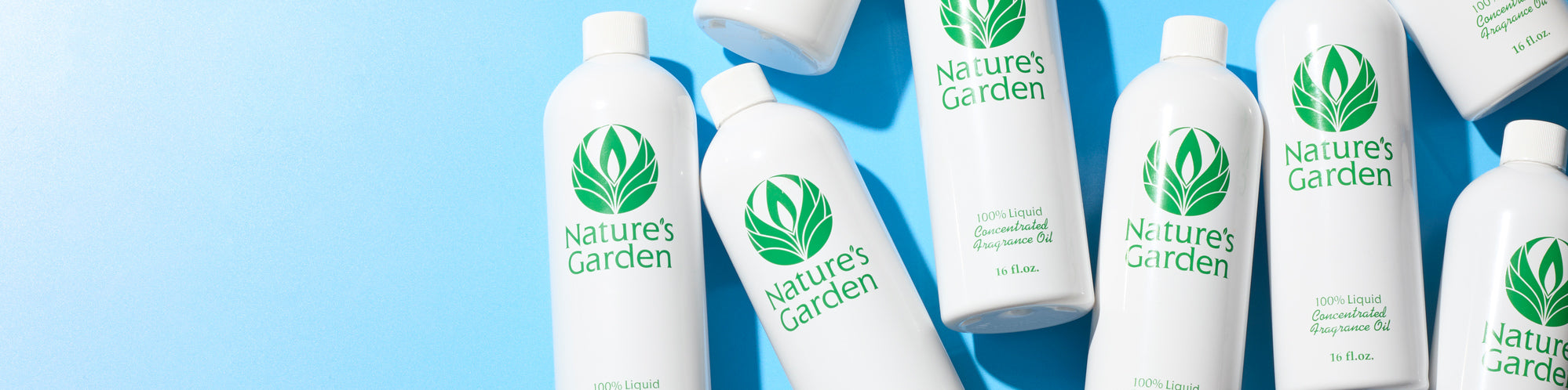 White Nature's Garden fragrance oil bottles arranged on a bright blue background, with green leaf logos and product labels visible. Wide banner layout with open space on the left for text.
