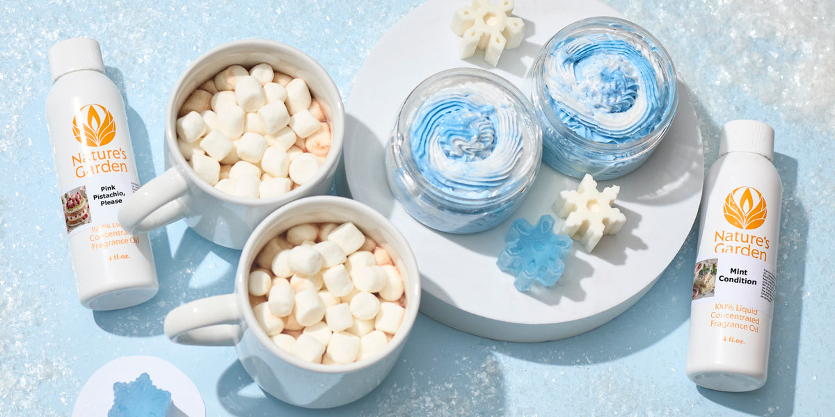 Nature’s Garden Pink Pistachio, Please and Mint Condition fragrance oils beside two mugs topped with marshmallows, blue-and-white whipped products, and snowflake shapes on an icy blue backdrop.