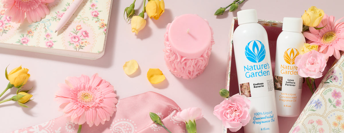Nature's Garden fragrance oil bottles in Endless Reverie and Love Letters Forever displayed with a pink decorative candle, pink gerbera daisies, yellow roses, carnations, floral notebooks, and a pink scarf on a soft pastel background.