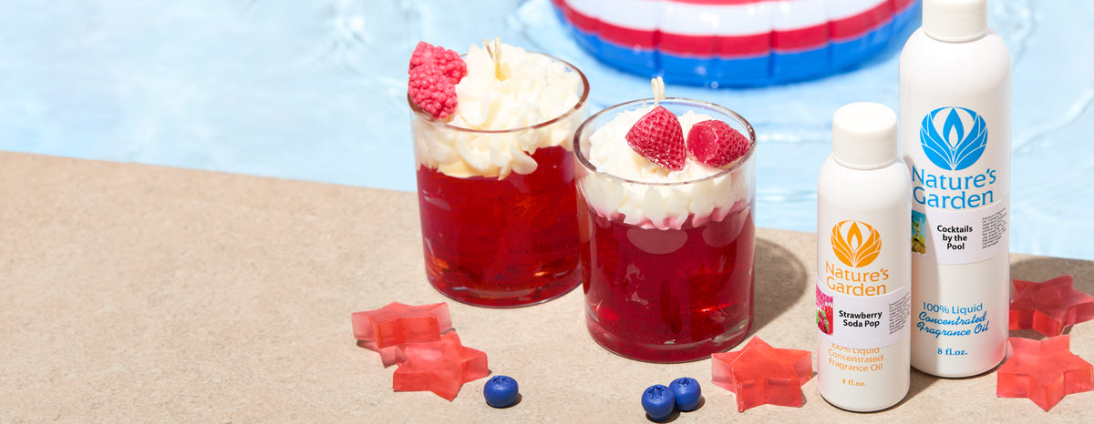 Red layered candles topped with whipped wax and berry accents alongside Nature’s Garden fragrance oil bottles near a swimming pool.