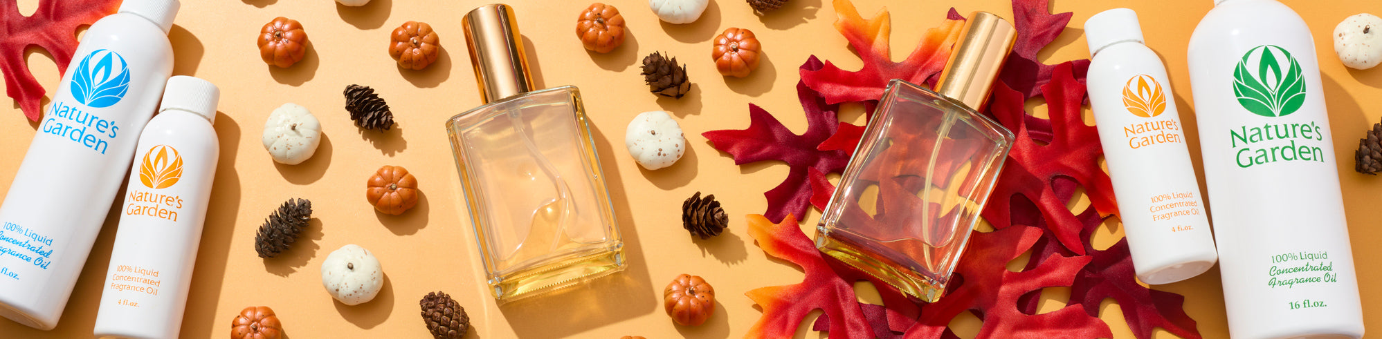 Nature's Garden fragrance oil bottles and clear perfume spray bottles arranged with red autumn leaves, mini pumpkins, white gourds, and pinecones on a warm golden background, creating a seasonal fall product display.