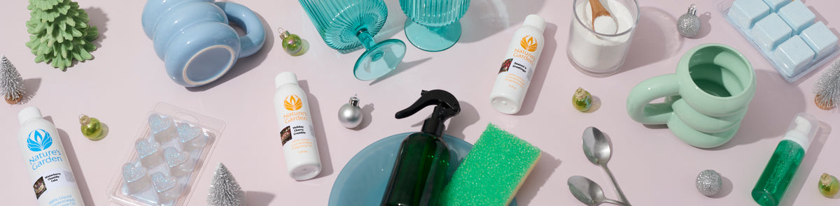 Holiday cleaning supplies and décor arranged on a pale pink surface, including Nature’s Garden cleaners, spray bottle, sponge, mugs, glasses, ornaments, and wax melts.